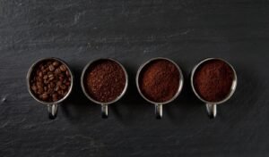 A mug of coffee beside a small pile of ground coffee beans.