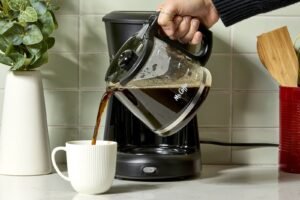 A steaming mug and coffee brewing tools on a wooden kitchen counter.