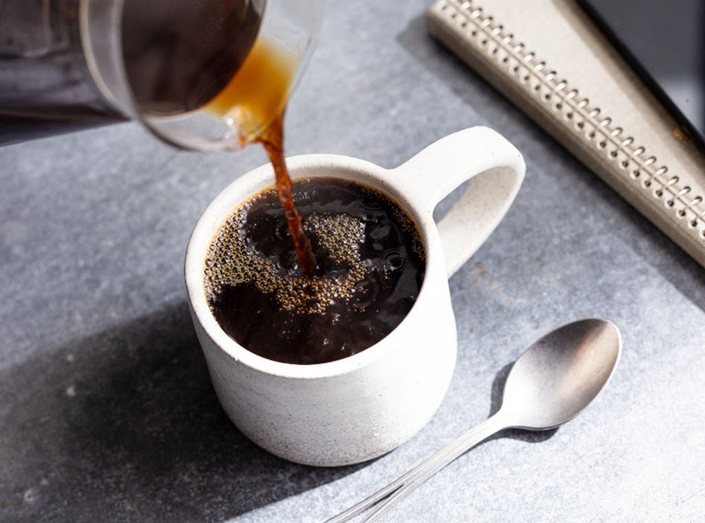 A fresh cup of medium roast coffee with beans on a kitchen counter.