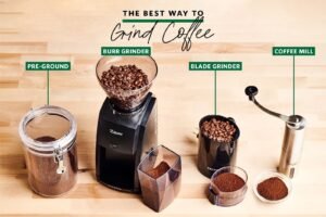 Freshly roasted coffee beans sit next to a professional burr grinder on wood.