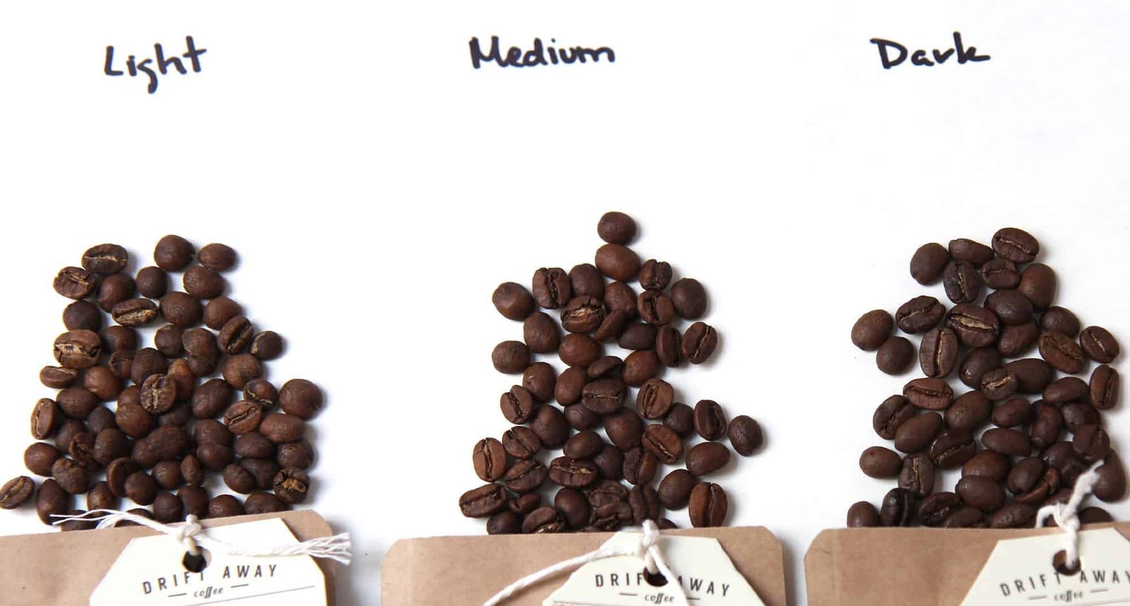 Three piles of coffee beans in different roast levels on a marble surface.