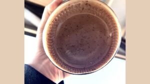 A mug of coffee showing sediment at the bottom on a wooden table.