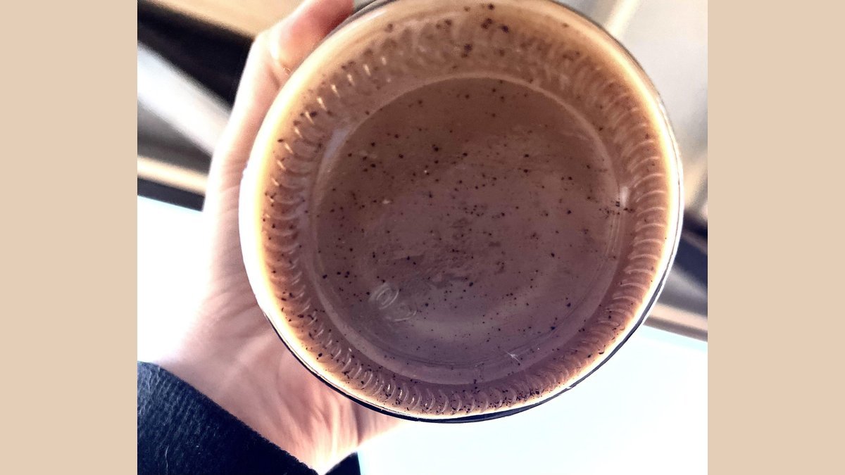 A mug of coffee showing sediment at the bottom on a wooden table.