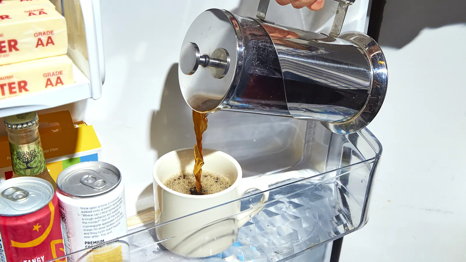 Dark brewed coffee being poured from a metal pot into a glass jar.