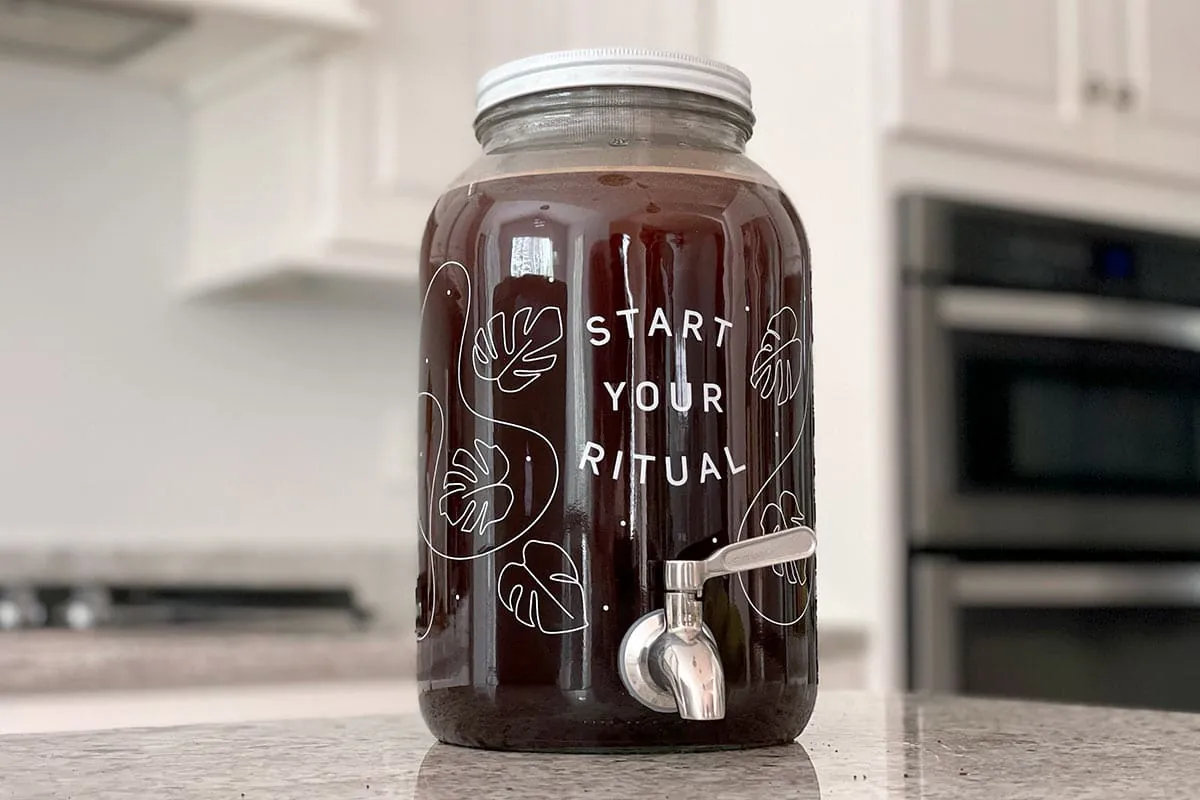 Glass jar of coffee grounds steeping in water inside a bright refrigerator.