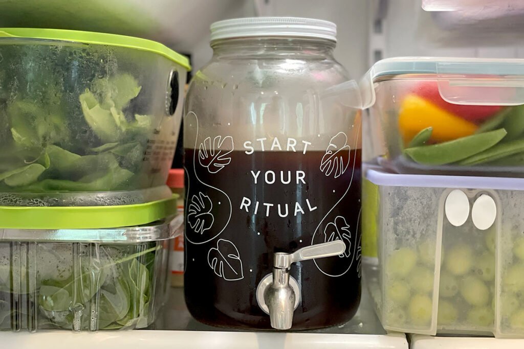Glass jar of cold brew coffee beside open refrigerator on marble counter