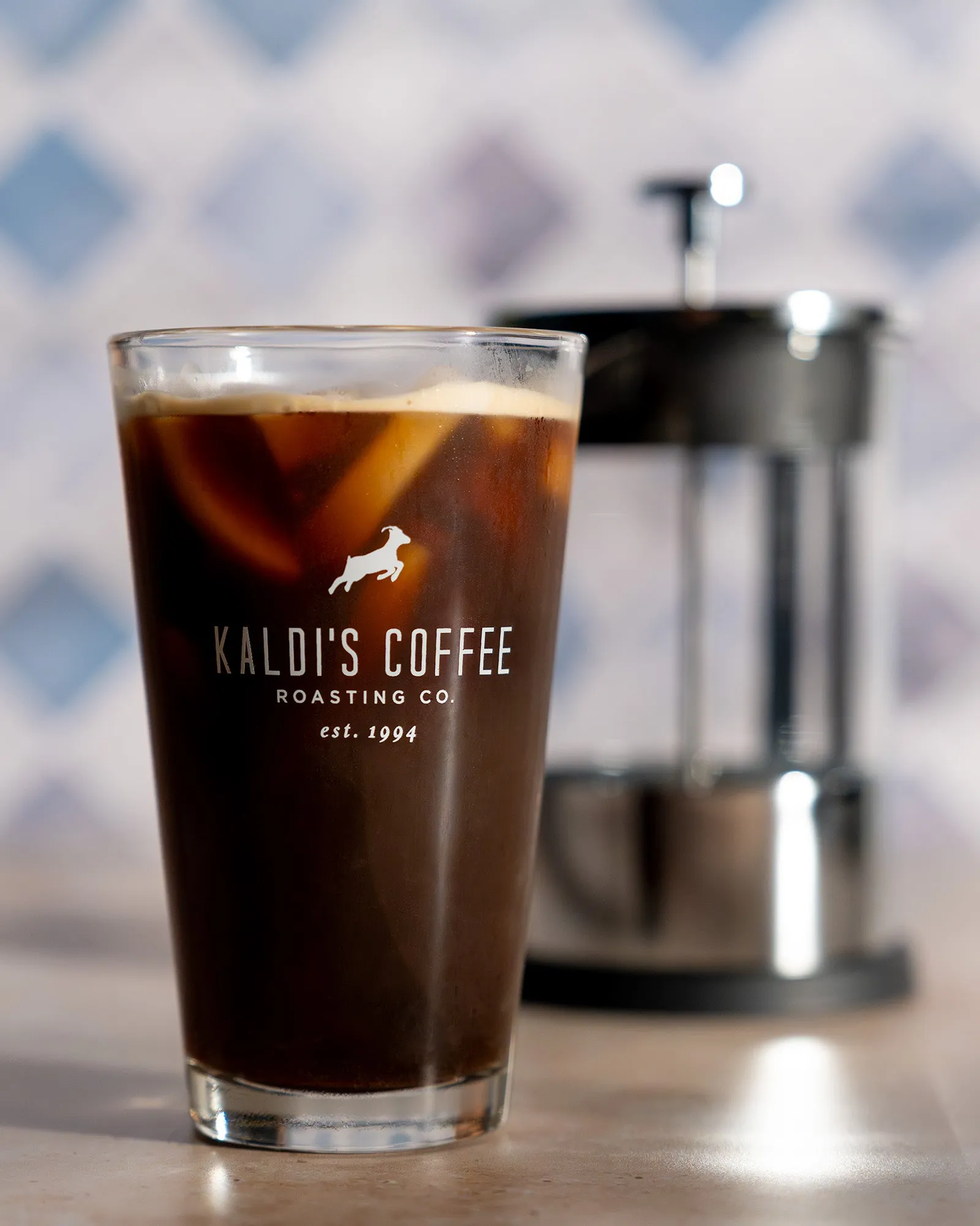 Hands removing a jar of steeping cold brew from a commercial refrigerator.