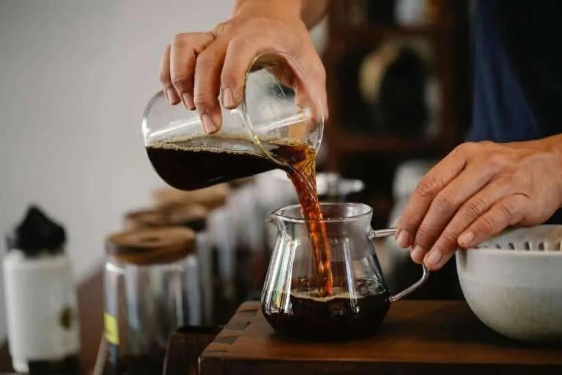 Pour-over dripper with fresh grounds sitting over a carafe of brewed coffee.