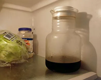 A sealed glass jar of brewed coffee stored inside a bright refrigerator.